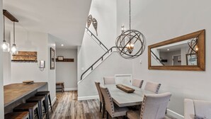 Een moderne eethoek met een houten tafel en stoelen, een hanglamp en een trap die naar een andere kamer leidt.