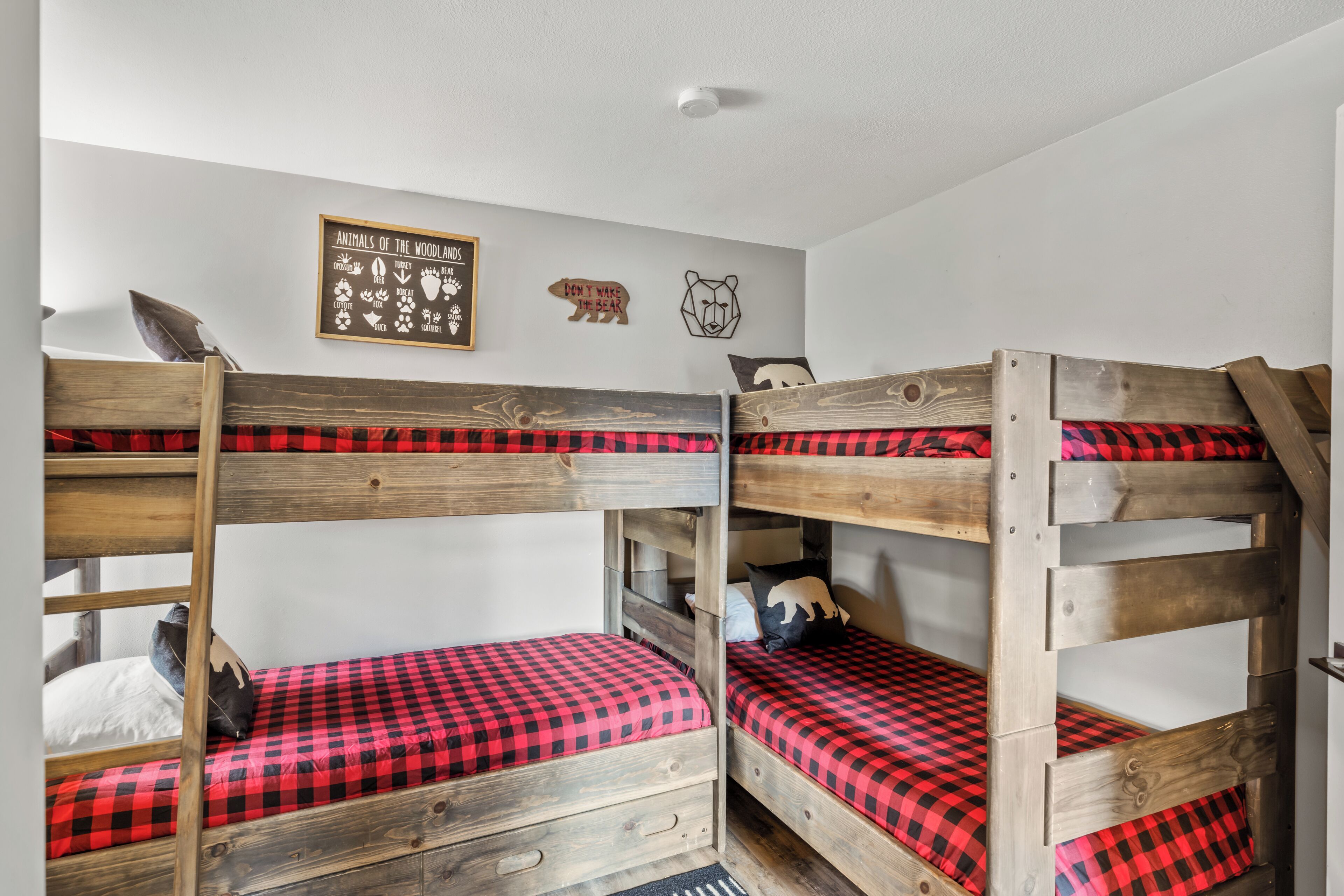 A bunk bed room with red and black checkered bedding, wooden bunk beds, and a wall with animal-themed decorations.