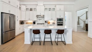 A modern kitchen with white cabinetry, a stainless steel refrigerator, a marble backsplash, and a central island with bar stools.