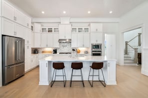 Una cocina moderna con armarios blancos, un refrigerador de acero inoxidable, un salpicadero de mármol y una isla central con taburetes de bar.