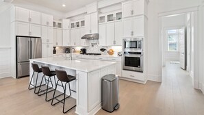 A modern kitchen with white cabinetry, stainless steel appliances, and a central island with bar stools.