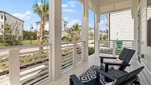 A covered porch with white railings, two black lounge chairs, and a patterned rug.