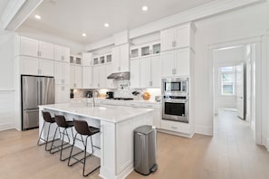 Una cocina moderna con armarios blancos, electrodomésticos de acero inoxidable y una isla central con taburetes de bar.