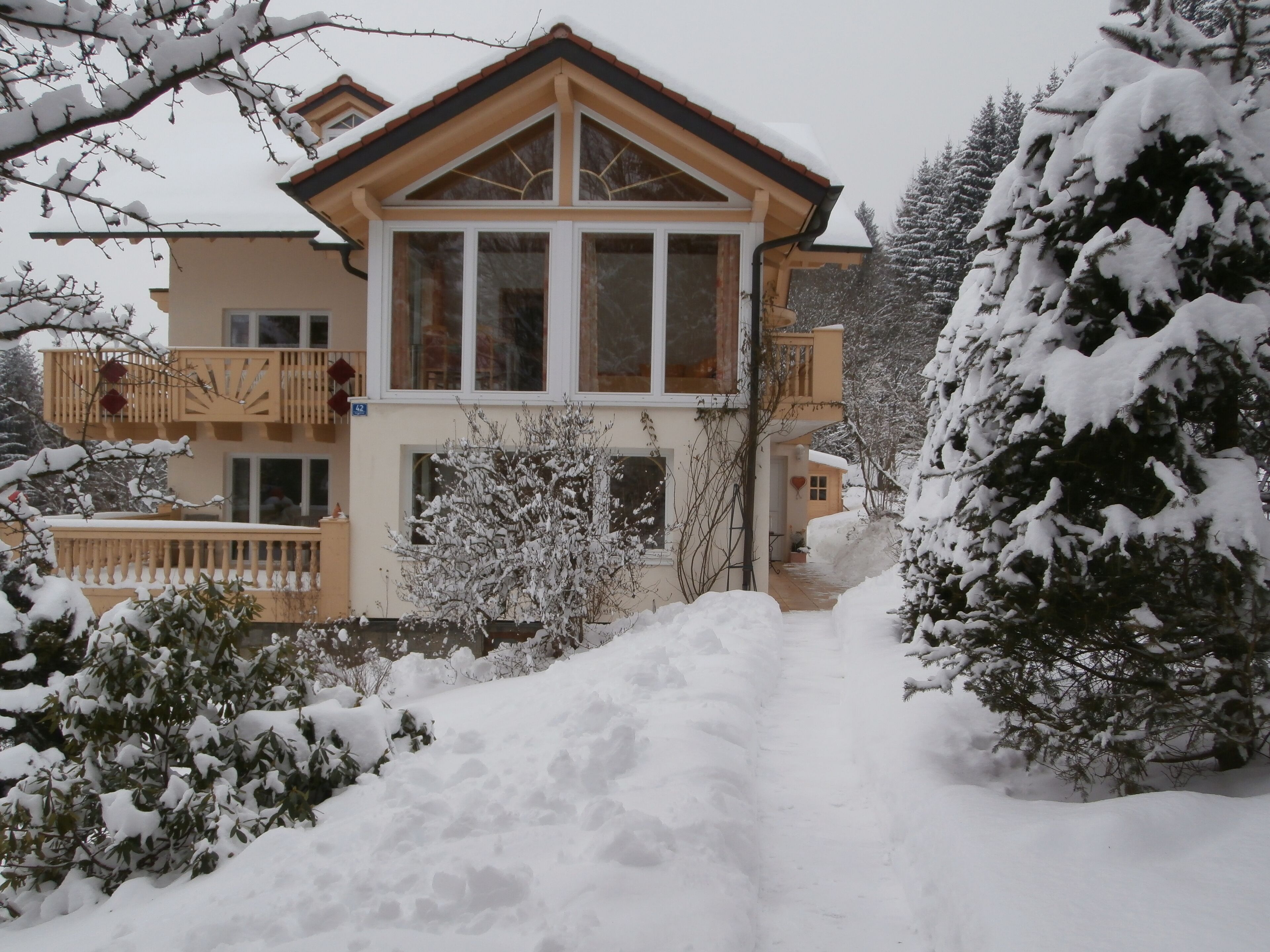 Een gebouw met twee verdiepingen, met een balkon op de tweede etage, omgeven door met sneeuw bedekte bomen en een sneeuwbedekte pad naar de ingang.
