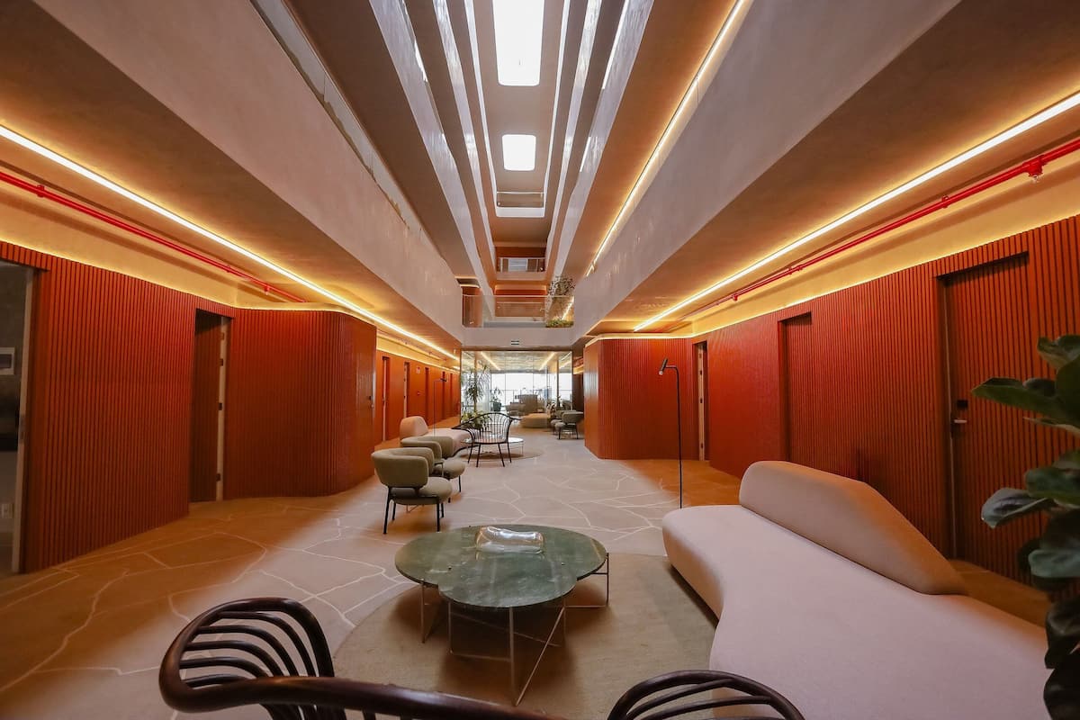 A modern hotel lobby with a central seating area, a staircase, and a view of the lobby in the background.
