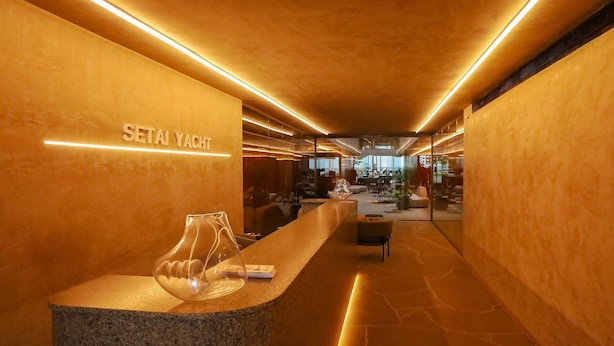 Uma área de recepção com balcão de pedra, um vaso de vidro e uma placa com a inscrição "SETAI YACHT".