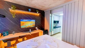 A modern hotel room with a bed, a desk, a TV, and a bathroom visible through an open door.