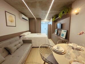 A modern hotel room with a bed, sofa, dining table, and chairs. - Setai Yacht Premium - By Almare Flats (João Pessoa)