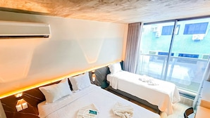 Quarto de hotel com uma cama, mesa de cabeceira, pequena mesa, ar condicionado e janela com vista.