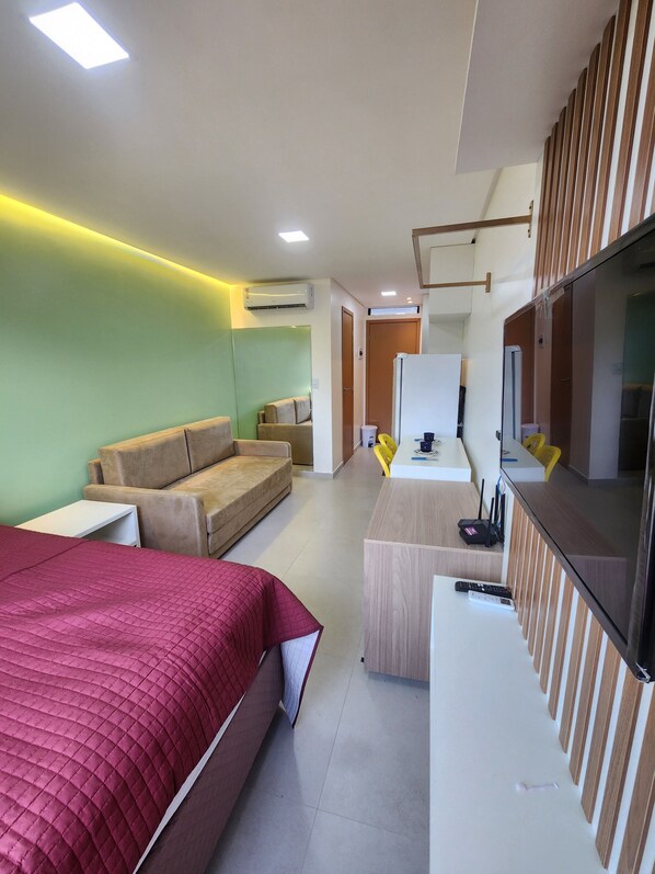A modern hotel room with a large bed, a sofa, a desk with a computer, and a TV.
