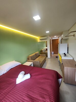 A hotel room with a large bed, a sofa, a desk, and a kitchenette.