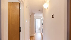 A narrow hallway with a wooden door on the left, a light fixture on the right, and a white wall with a small picture frame.