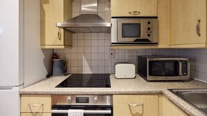 A kitchen with a built-in stove, two wall-mounted microwaves, a toaster, and a stainless steel range hood.