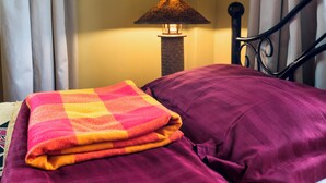 A bed with a purple blanket and a checkered blanket, a lamp, and curtains. - Poolside 2-Bedroom Apartment with heated pool at the Jungle Oasis (Nairobi)