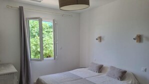 Une chambre avec un grand lit, une fenêtre avec des rideaux, une table de chevet et une lampe fixée au mur.