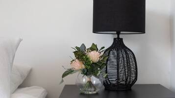 A black lamp with a woven base on a black nightstand next to a clear vase with flowers.