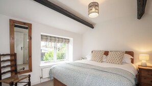 A bedroom with a wooden bed, a nightstand, a chair, a window with a view, and a hanging light fixture.