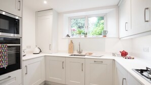 A modern kitchen with white cabinetry, a built-in oven, a sink, and a window with a view of greenery.