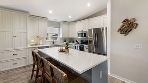 A modern kitchen with white cabinetry, a large island, stainless steel appliances, and a herringbone-patterned backsplash. - Bean Point Bliss 3 Bedroom Home by RedAwning (Anna Maria)