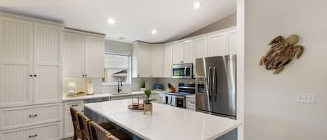 Una cocina moderna con armarios blancos, una isla grande, electrodomésticos de acero inoxidable y un backsplash con estampado en espiga.