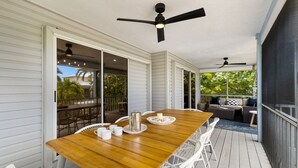 A covered patio with a wooden table and white chairs, a ceiling fan, and a view of the outdoors. - Bean Point Bliss 3 Bedroom Home by RedAwning (Anna Maria)