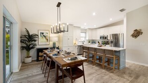A modern kitchen with white cabinets, stainless steel appliances, and a wooden dining table with chairs. - Bean Point Bliss 3 Bedroom Home by RedAwning (Anna Maria)