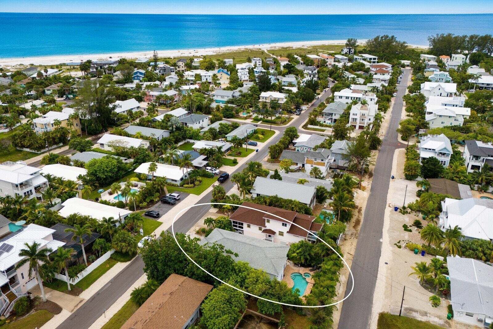 An aerial view of a coastal residential area with houses, roads, and a beach.