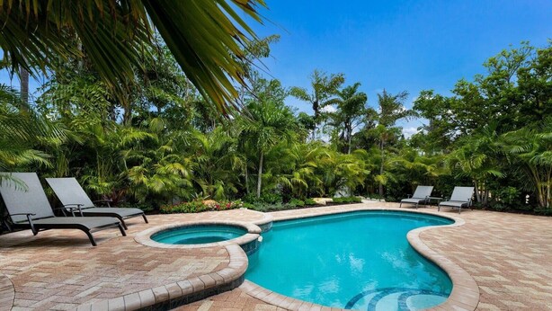 A swimming pool with two hot tubs, surrounded by lounge chairs and lush tropical vegetation. - Bean Point Bliss 3 Bedroom Home by RedAwning (Anna Maria)