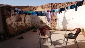 Un patio con dos sillas de mimbre, un tendedero con ropa variada y un taburete pequeño.