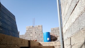 Una obra en construcción con paredes de hormigón sin terminar y un barril azul.