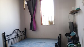 Una habitación pequeña con cama individual, ventana, estante en la pared con un ventilador y un enchufe.