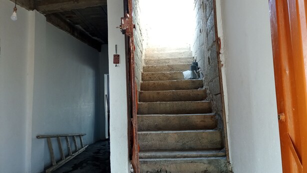 Una escalera que conduce a un espacio luminoso, con barandilla de metal y una puerta de madera a la derecha.
