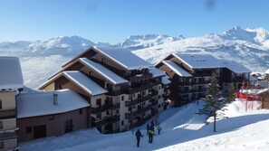Estância de esqui coberta de neve, com edifícios altos, pistas de esqui e montanhas ao fundo.