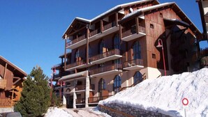 Un edificio de madera de varios pisos con balcones, una base de piedra y una pista de esquí al frente.