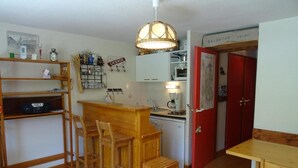 Cocina compacta con barra de madera, taburetes, máquina de café y una puerta roja con la etiqueta 'BARBECUE'.
