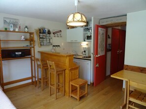 Cuina compacta amb un taulell de bar de fusta, tamborets, una màquina de cafè i una porta vermella amb la inscripció "BARBECUE".