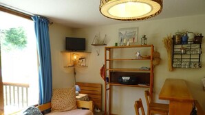 Una habitación acogedora con una cama, un escritorio y una silla. Se observa una estantería con diversos objetos y una ventana con cortinas.