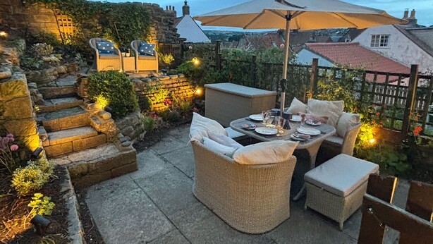 An outdoor patio with wicker furniture, a table set for dining, and a large umbrella providing shade.