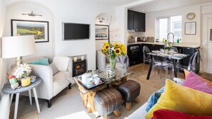 A modern living room with a fireplace, a dining area with clear chairs, and a kitchen with dark cabinets.