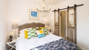 A neatly arranged bedroom with a bed, bedside lamps, a chandelier, a mirror, and a framed picture on the wall.