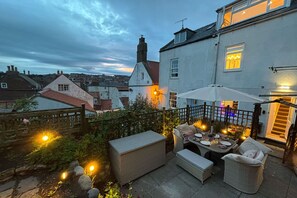 An outdoor patio with wicker furniture, a table set for dining, and string lights. - Host & Stay | Voyagers' View (Whitby)