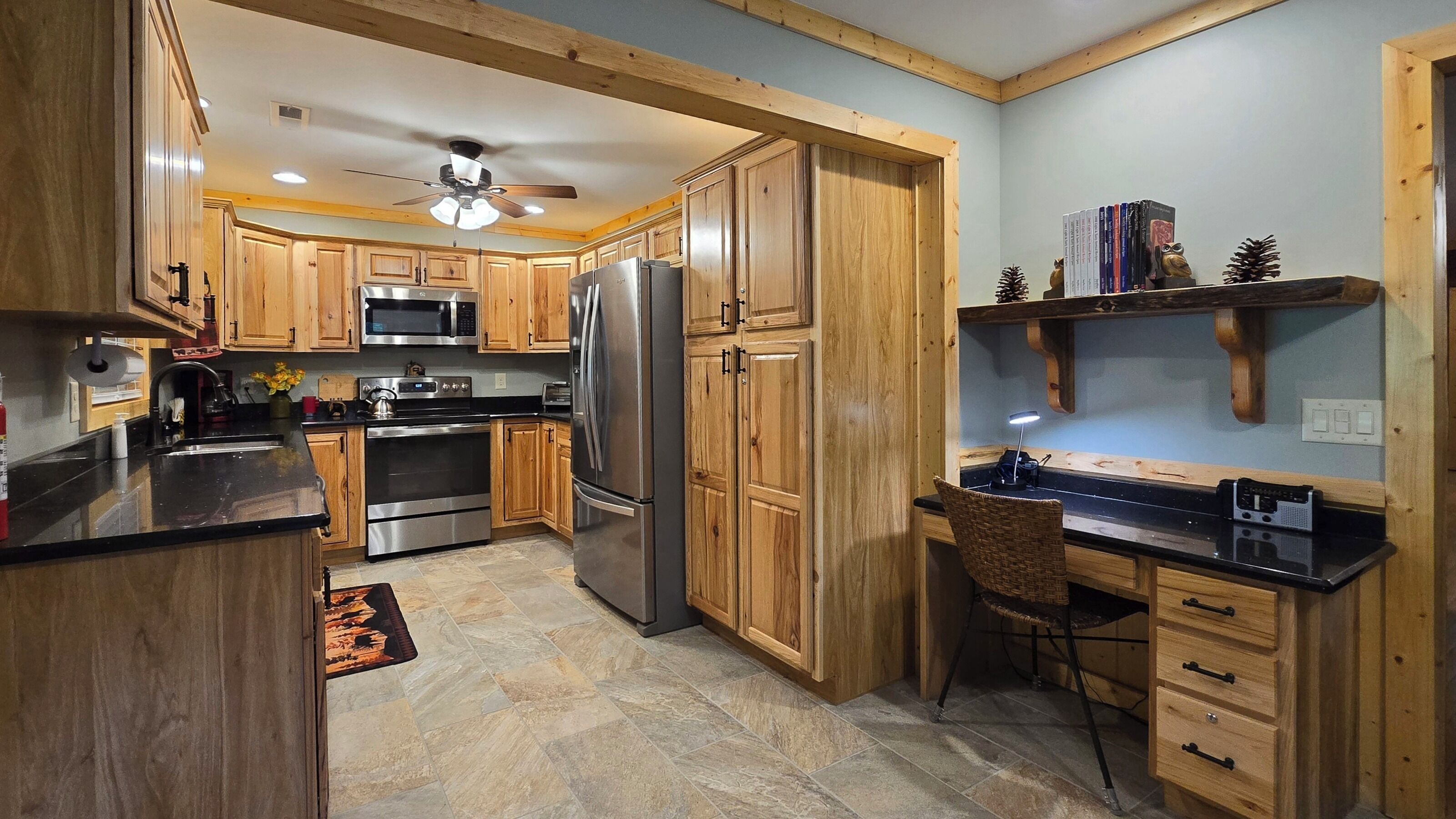 A kitchen with wooden cabinets, stainless steel appliances, a black countertop, and a ceiling fan.