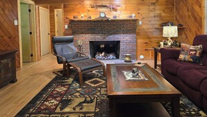 A cozy living room with a brick fireplace, leather armchair, and a patterned rug. - Yellow Creek Cabin (Robbinsville)