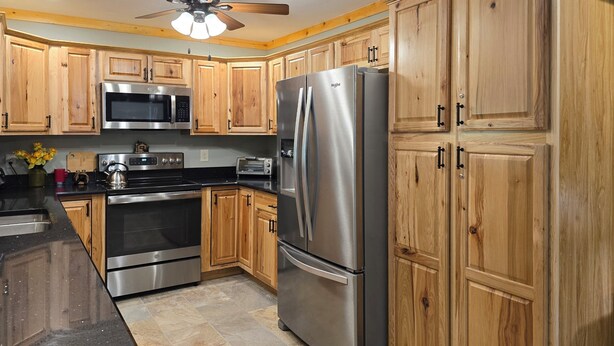 A kitchen with wooden cabinets, stainless steel appliances, a microwave, oven, toaster, and a refrigerator. - Yellow Creek Cabin (Robbinsville)