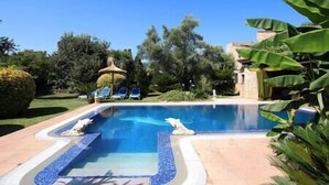A swimming pool with lounge chairs and a thatched umbrella.
