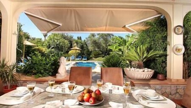 A dining area with a view of a swimming pool, surrounded by lush greenery and a statue.