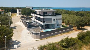A modern multi-story building with a rooftop pool, surrounded by greenery and overlooking a body of water. - Villa Loreta with pool, barbeque and sea view. (Pula)