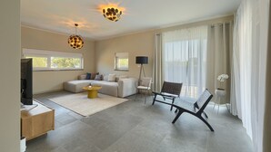 A modern living room with a sectional sofa, a coffee table, a TV, and a floor lamp. There are large windows with curtains and a view of the outdoors. - Villa Loreta with pool, barbeque and sea view. (Pula)