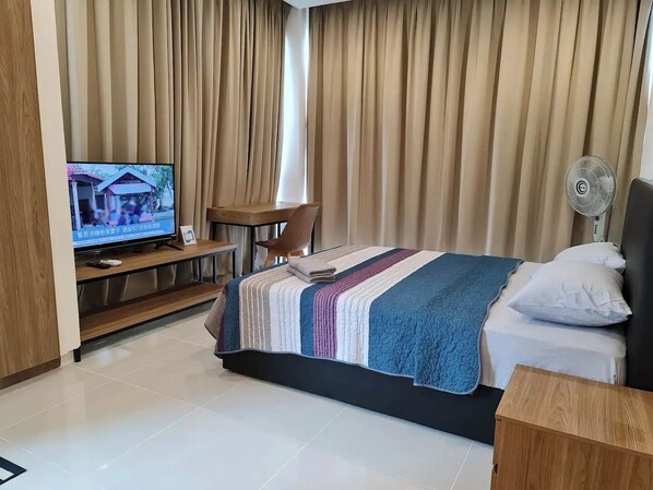 A hotel room with a bed, a desk, a chair, a TV, and a standing fan. - Cozy Home 1 @Kozi Square near General Hospital


 (Kuching)