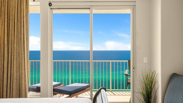 A hotel room with a balcony overlooking the sea, a bed, a chair, and a small table. - Gulf-front escape w/ tickets, pool & hot tub (Panama City Beach)
